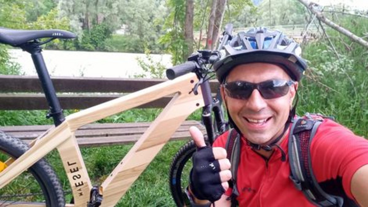 Foto Gewinner E-Bike Das Foto zeigt einen Mann mit Sonnenbrille und Radhelm, der mit einem E-Bike aus Holz im Wald unterwegs ist.