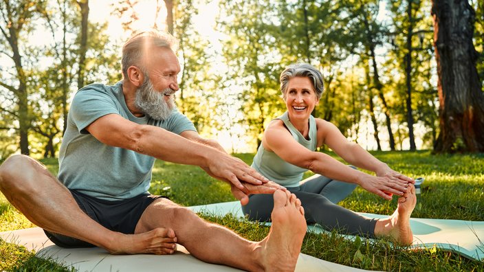 Älteres Ehepaar beim Yoga im Park Das Bild zeigt ein älteres Ehepaar auf Yogamatten sitzend, bei Dehnungsübungen.