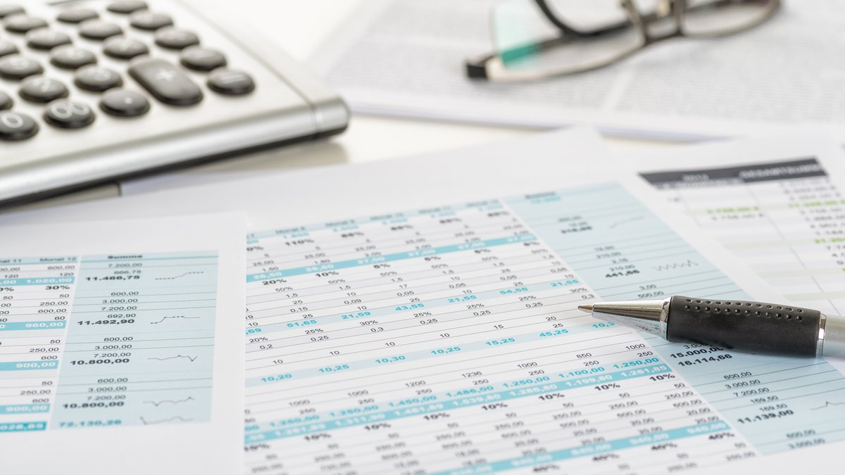 Afrac Stellungnahme 27_2022 Nahaufnahme von Finanzunterlagen mit Tabellen und Zahlen, daneben ein Kugelschreiber, ein Taschenrechner und eine Brille auf einem aufgeschlagenen Dokument