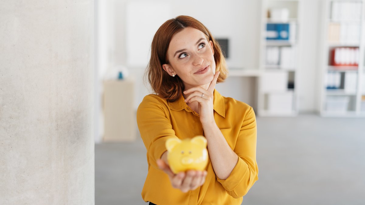 Geschäftsfrau mit Sparschwein Eine junge Frau in einer gelben Bluse sieht nachdenklich nach oben. In ihrer Hand ist ein gelbes Sparschwein