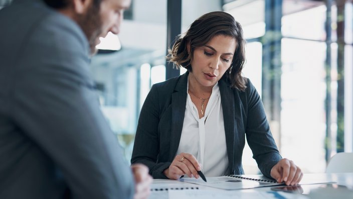 Professionelles Beratungsgespräch Das Bild zeigt eine Frau und einen Mann in einer Gesprächssituation. Vor der Frau liegen Unterlagen, auf die sie mit einem Stift zeigt.